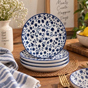 Puede incluir: Una pila de cuatro platos redondos de cerámica con base blanca y un patrón repetitivo de enredaderas florales en azul oscuro. Los platos tienen un acabado liso y brillante con un borde ligeramente elevado y un diseño botánico.