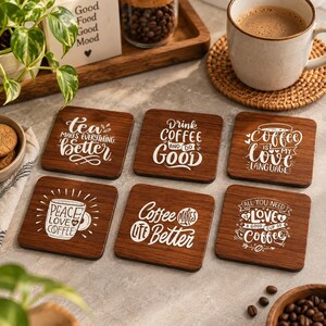May include: A set of six square dark wood coasters featuring white printed text and graphics. The designs include phrases such as tea makes everything better, drink coffee and do good, coffee is my love language, peace love coffee, coffee makes life better, and all you need is love and a good cup of coffee.