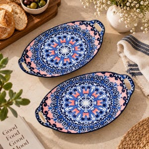 May include: Two oval ceramic serving platters featuring a vibrant blue, white, and coral pink mandala-inspired pattern. Each platter has integrated side handles and a decorative border with intricate scrollwork and a fine grid texture.