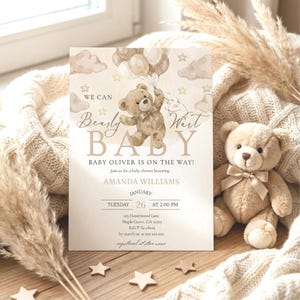 Peut inclure: Une invitation de baby shower avec une illustration d'ours en peluche tenant des ballons. Le texte dit "We can bearly wait BABY" et comprend les détails d'une baby shower en l'honneur d'Amanda Williams. Un ours en peluche est également visible.