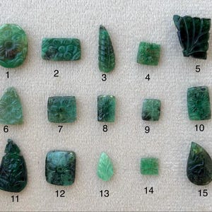 May include: Fifteen carved emerald gemstones with floral and leaf patterns. The collection includes various shapes, such as oval, rectangular, leaf, and square. The gemstones display detailed carvings and different shades of green.