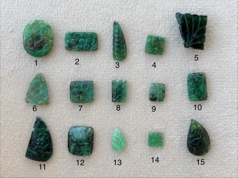 May include: Fifteen carved emerald gemstones with floral and leaf patterns. The collection includes various shapes, such as oval, rectangular, leaf, and square. The gemstones display detailed carvings and different shades of green.