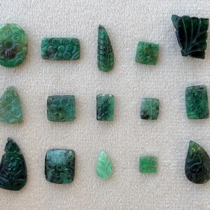 May include: A selection of carved emerald gemstones in diverse shapes, such as oval, rectangular, and leaf-like. Each gemstone displays detailed floral or leaf patterns, highlighting the natural green hue and intricate craftsmanship.