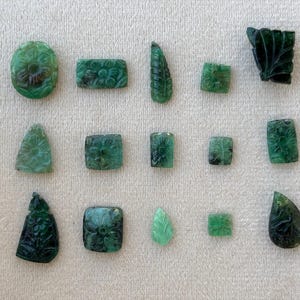 May include: A selection of carved emerald gemstones in diverse shapes, such as oval, rectangular, square, and teardrop. The gemstones display floral and leaf patterns, highlighting intricate details and a deep green hue.