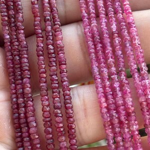 Può includere: Primo piano di diversi fili di piccole perline di pietre preziose sfaccettate color rubino. Le perline sono infilate insieme, mostrando variazioni di colore dal rosso intenso al rosa chiaro. Le pietre preziose hanno una forma leggermente irregolare e una finitura lucida.