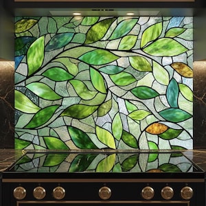 Può includere: Una backsplash decorativa per la cucina con un design a vetrata di foglie e rami verdi. Le foglie variano in tonalità di verde, con alcuni accenni di giallo e marrone. Installata sopra un piano cottura nero.