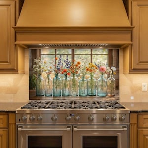 May include: A row of clear glass bottles filled with colorful wildflowers. The bottles are arranged on a wooden surface in front of a window. The kitchen features a stainless steel stove and wooden cabinets.