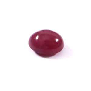 Puede incluir: Una gema pulida, de forma ovalada y color burdeos intenso. La superficie lisa refleja la luz, creando reflejos. La gema se encuentra sobre un fondo blanco, resaltando su color y forma. Adecuada para la creación de joyas.