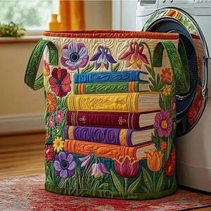 May include: A quilted laundry hamper featuring a stack of colorful books and vibrant floral designs. The hamper has green handles and a red trim, with a detailed pattern of flowers and leaves. The background is a neutral beige.