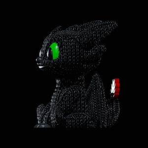 Puede incluir: Una figura de dragón negro con ojos verde brillante y una aleta caudal roja y blanca. El dragón está hecho de un material tejido y el fondo es negro.