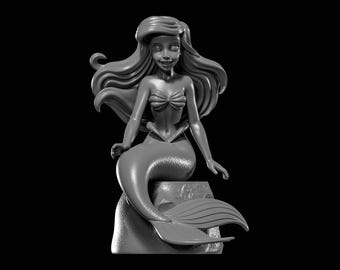 May include: A grayscale sculpture of a mermaid with long flowing hair, a seashell top, and a fishtail. The mermaid is seated on a rock, with her arms resting at her sides. The sculpture is set against a black background.