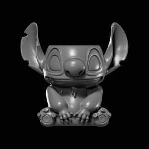 May include: A grey, 3D-printed figurine of the character Stitch from the Disney film Lilo & Stitch. The figurine is seated with arms crossed and large ears extending upwards. The figure has a large nose and closed eyes.