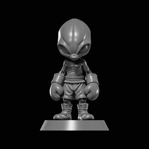 May include: A gray, stylized figurine of an alien boxer. The alien has a large head, big eyes, and is wearing boxing gloves, shorts, and boots. The figure is standing on a rectangular base against a black background.