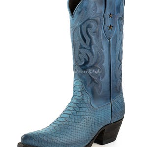 Può includere: Stivale da cowboy blu con punta affilata e motivo a pelle di serpente sulla parte del piede. La parte superiore dello stivale presenta disegni floreali in rilievo e due stelle. Il tacco è nero.