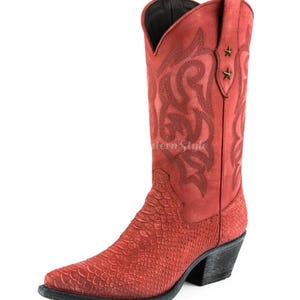 Op de afbeelding: Rode cowboylaars met een puntige neus en een getextureerde schacht. De laars heeft decoratieve stiksels en twee stervormige accenten aan de bovenkant. De hak is zwart en de laars is van leer.