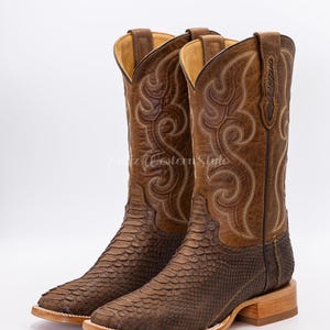 Könnte beinhalten: Ein Paar braune Cowboy-Stiefel mit einem strukturierten Schlangenmuster am unteren Teil und einem gestickten Design am oberen Schaft. Die Stiefel haben eine quadratische Spitze und eine hellfarbige Sohle.