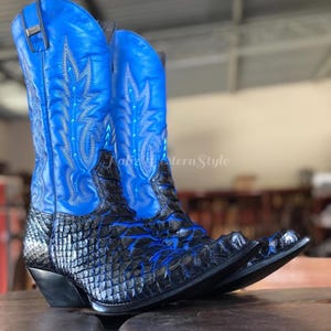 May include: A pair of cowboy boots with a striking blue and black design. The upper part of the boots is a vibrant blue with decorative stitching, while the lower part features a textured black pattern. The boots have pointed toes and a classic western style.