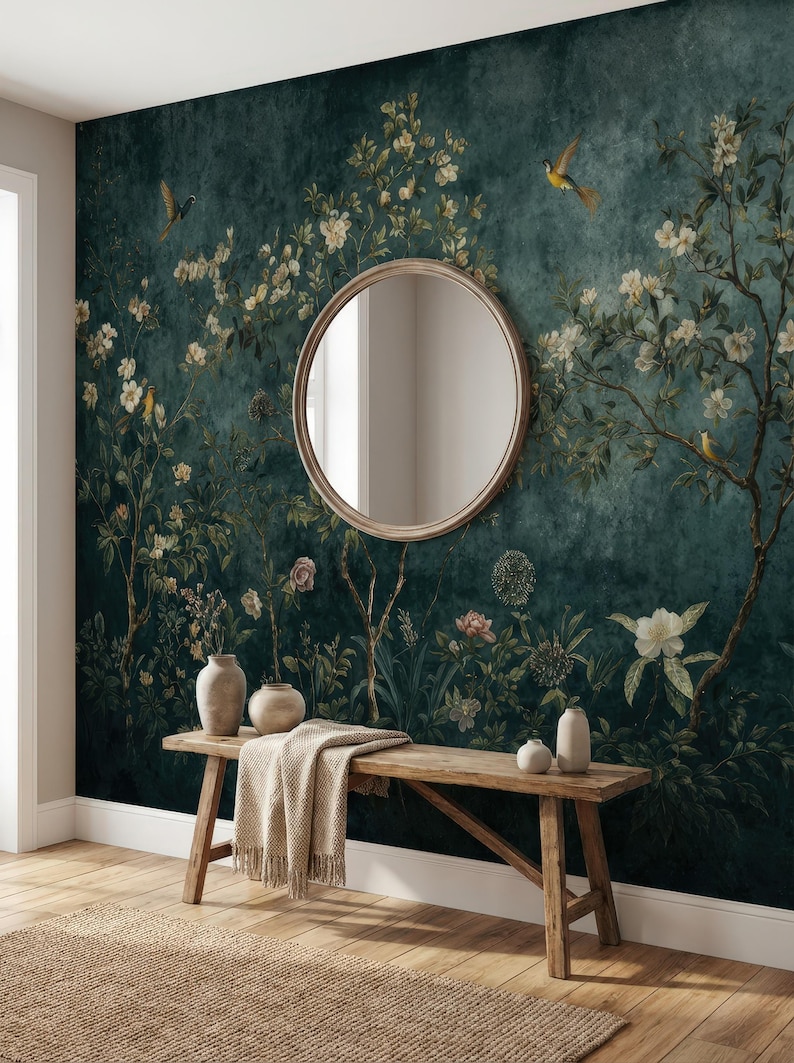 May include: A dark teal floral wallpaper with a round mirror, wooden bench, and vases. The wallpaper features white flowers, birds, and foliage. A beige throw blanket rests on the bench, and a woven rug is on the floor.