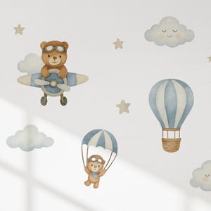 May include: A set of wall decals featuring watercolor illustrations of brown teddy bears in aviator goggles. One bear flies a blue and white airplane, another descends with a blue and white parachute. Includes blue and white hot air balloons and clouds.