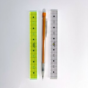 May include: Two clear plastic rulers with black markings and a bee design, and an orange mechanical pencil with a black eraser.