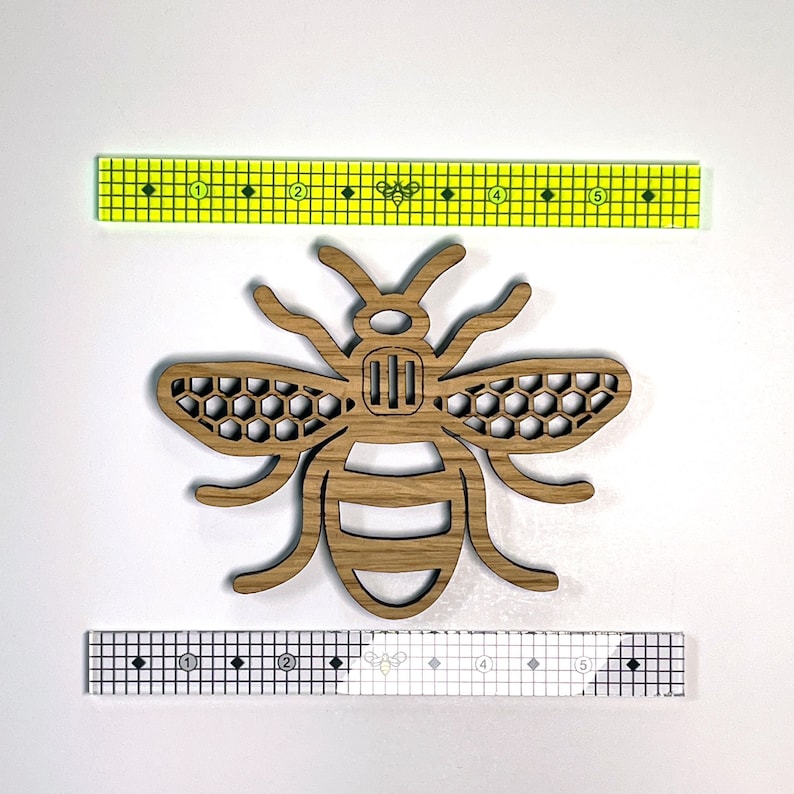 May include: A wooden cutout of a bee with a honeycomb pattern on its wings. The bee is brown and has a black outline. The bee is approximately 2 inches wide.