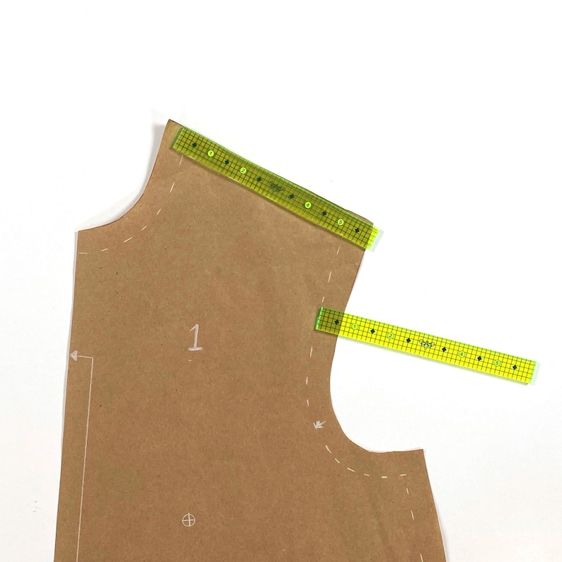 May include: A brown paper pattern with two green rulers, one placed along the top edge and the other placed diagonally across the pattern. The pattern has markings and the number "1" written on it.
