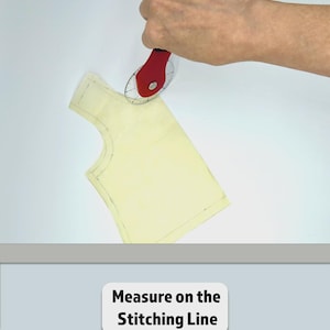 Puede incluir: Un cortador rotatorio rojo con un mango negro mide un patr&oacute;n de tela amarilla. El texto "Measure on the Stitching Line" se muestra sobre un fondo blanco.