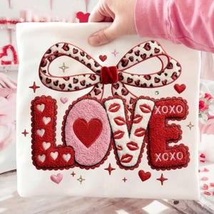 May include: White fabric with a large bow and the word "LOVE" in red, pink, and white. The bow has a leopard print pattern with red hearts. The letter "O" is pink with a red heart. The letter "V" has red lips.