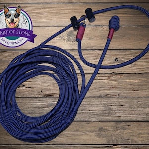May include: A navy blue rope dog leash featuring a slip lead design with two black cylindrical sliders, a metal ring, and a decorative knot at the end. The leash includes maroon-colored accents near the sliders and the knot, with a logo.