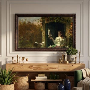 Op de afbeelding: Een ingelijst olieverfschilderij met een persoon in een witte blouse in een stenen deuropening met vogels, geplaatst boven een lichthouten sidetable met gevlochten manden, groene planten en donkerblauwe keramische vazen.