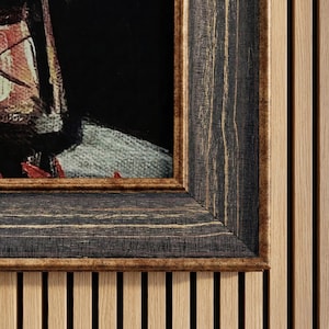 以下が含まれることがあります： 暗く、質感のある木製フレームに入った絵画のクローズアップ。フレームの内側は金色の縁取り。絵画は、赤と白のアクセントのある顔の一部を特徴としています。背景は黒です。