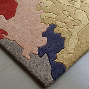 May include: A colorful area rug with an abstract design. The rug features a mix of colors, including red, pink, blue, and tan, creating a unique and artistic pattern. The rug's texture appears soft and inviting, suitable for a living space.