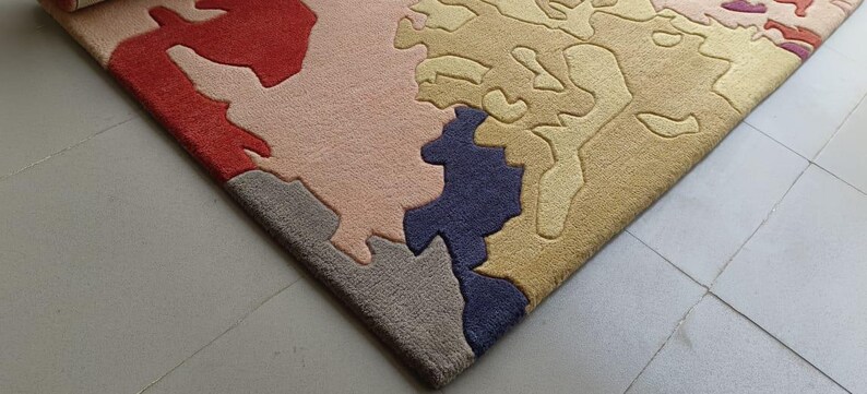 May include: A colorful area rug with an abstract design. The rug features a mix of colors, including red, pink, blue, and tan, creating a unique and artistic pattern. The rug's texture appears soft and inviting, suitable for a living space.