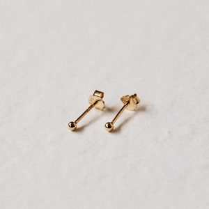 May include: A pair of small, gold stud earrings with a round ball at the end of each post.