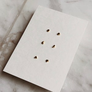 May include: A set of six gold-toned earrings with different geometric shapes, including circles, crescents, and triangles. The earrings are displayed on a white card.