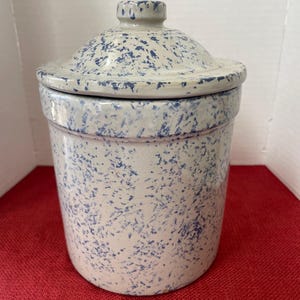 May include: A ceramic jar with a lid, featuring a speckled blue and white design. The jar has a cylindrical shape with a matching lid and a small knob. The overall aesthetic is rustic and vintage.