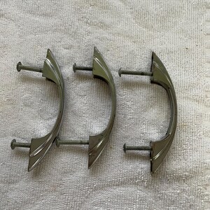 May include: Three silver-toned metal drawer pulls with a curved, arched design. Each handle features two attached threaded mounting screws extending from the back, intended for installation on furniture or cabinetry hardware.
