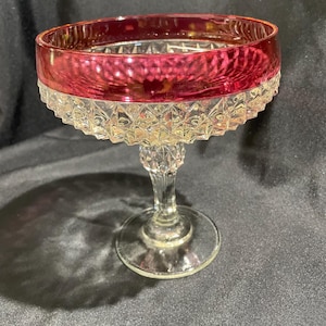 May include: A vintage champagne coupe glass with a ruby red rim and a clear, diamond-patterned base. The stem is clear and elegant, and the foot is a simple, round base. This elegant glass is perfect for serving champagne or cocktails.
