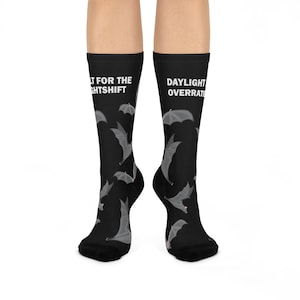 May include: Black socks with a pattern of gray bats and umbrellas. The text "WAIT FOR THE NIGHTSHIFT" and "DAYLIGHT OVERRATED" is printed on the socks. The socks are worn on a person's legs.
