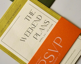 May include: A wedding invitation suite featuring a cream-colored card with black text reading THE WEEKEND PLANS APRIL 23 - 25 2026, overlaid with a bright orange RSVP band, all resting on a dark olive green envelope sealed with a gold wax stamp.