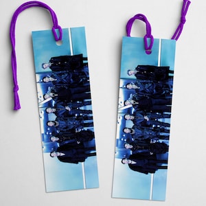 May include: Two rectangular bookmarks with a blue backdrop and a purple cord. The bookmarks display a mirrored image of people in black attire. A purple cord is attached at the top of each bookmark.