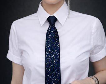 May include: A navy blue tie with a pattern of small, colorful dots. The tie is worn with a white collared shirt with rolled-up sleeves. The image is a close-up, focusing on the tie and shirt.