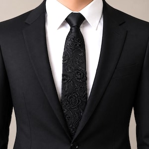 May include: A black suit jacket, white shirt, and black tie. The tie has a floral pattern. The suit is a classic design, suitable for formal events. The jacket is tailored.