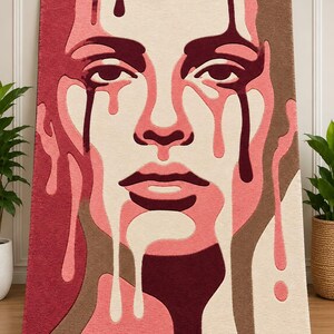 May include: A rectangular tufted rug featuring a stylized portrait of a face with dripping liquid elements. The design uses a color palette of deep burgundy, soft pink, cream, and muted brown tones, creating a layered, textured graphic effect.