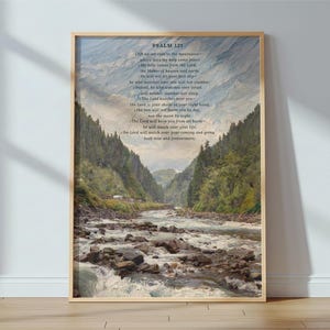 May include: A rectangular wall art print featuring a landscape painting of a rocky river flowing through a valley between forested mountains. The text Psalm 121 is printed at the top, followed by the full biblical passage in dark lettering.