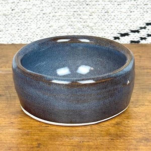 Könnte beinhalten: Eine handgefertigte Keramikschale mit dunkelblauer Glasur und braunem Rand. Die Schale hat eine abgerundete Form mit weißem Boden. Das Innere der Schale ist ein hellerer Blauton, und die Außenseite ist ein dunklerer Blauton.