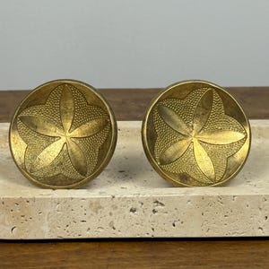 May include: A pair of antique brass cabinet knobs featuring a starfish design. The round knobs have a detailed, textured surface and a central starfish motif. The brass has a warm, aged patina, suggesting vintage or antique origins.