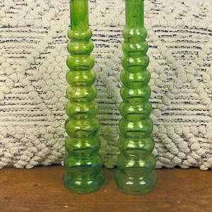 May include: Two green glass vases with a stacked, bulbous design. The vases are a vibrant green colour and have a long, slender neck. The vases are likely decorative items, suitable for displaying flowers or as standalone decor.