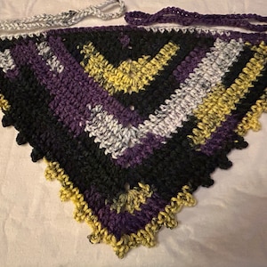 May include: A crocheted triangular scarf with a black, purple, white and yellow colour pattern. The scarf has a fringed edge.
