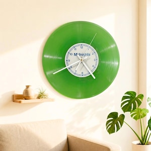 Può includere: Un orologio da parete circolare realizzato con un disco in vinile verde traslucido. L'etichetta centrale è bianca con numeri blu da 1 a 12 e la scritta Midnights stampata in blu. Presenta tre sottili lancette bianche che indicano l'ora.